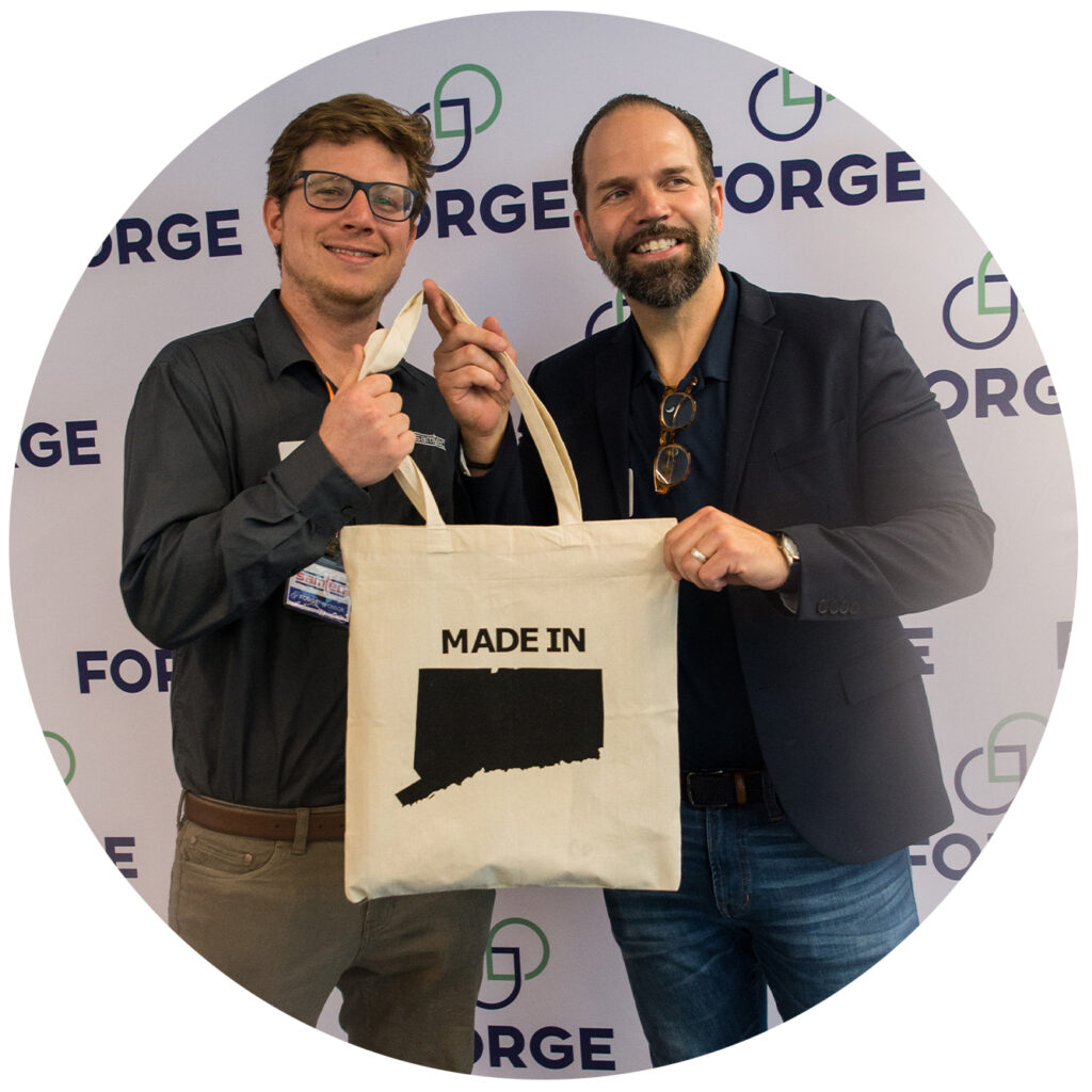Samtec Field Application Engineer Christian Rodriguez and FORGE Vice President Adam Rodrigues pose with a 'Made in Connecticut' tote bag.