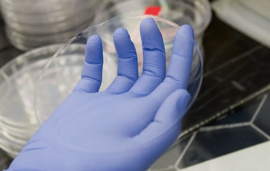 A gloved hand holds a circular sample of the Aeroshield clear aerogel material.