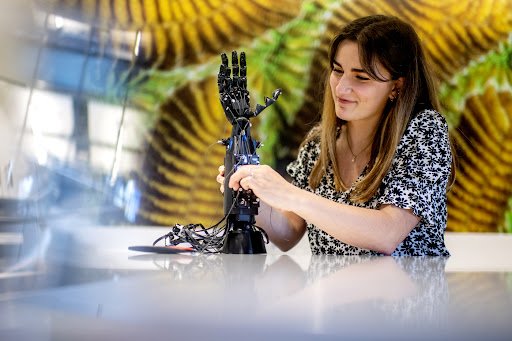 A woman squeezes the robotic hand's wrist with both of her hands