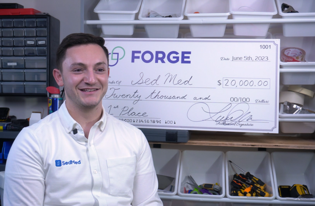 SedMed founder Jeremy Bronen in the workshop with an oversized funding check from FORGE